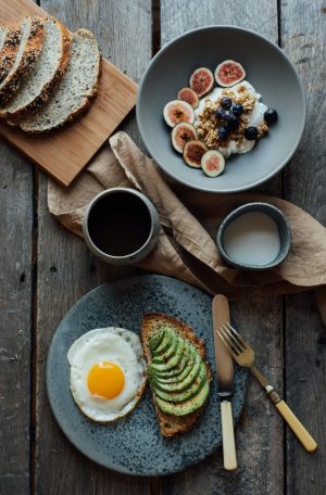 Healthy breakfast with avocado toast, eggs, and yogurt with figs and berries on a wooden table.